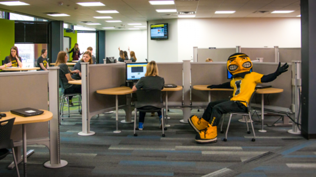 Herky sitting in a study area with UI students.